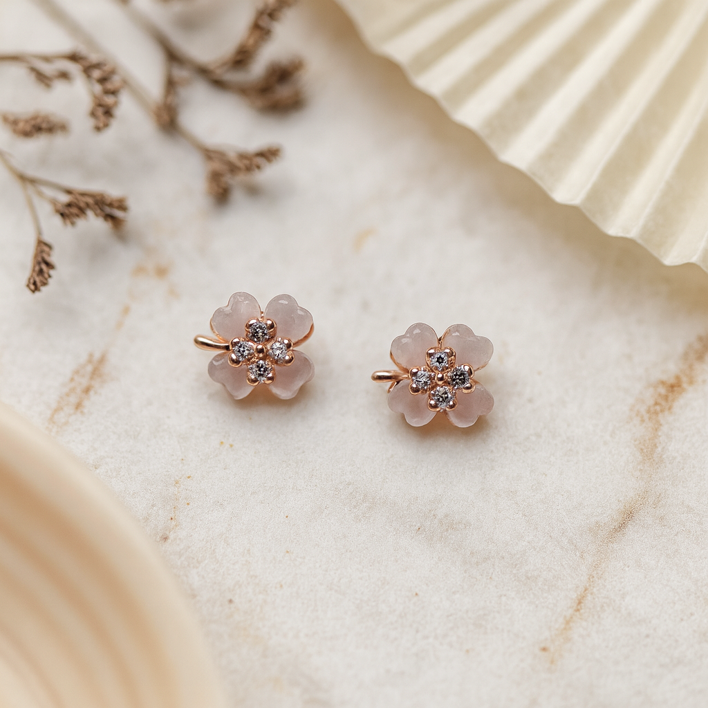 Pair of flower-shaped earrings with rose gold and clear gemstones on a marble surface.